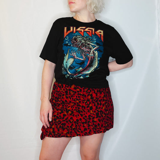 Blonde woman is wearing a black metal band style t-shirt and red leopard print skirt; the t-shirt shows an illustration of a skeleton siren under the sea and "VISSIA" across the top