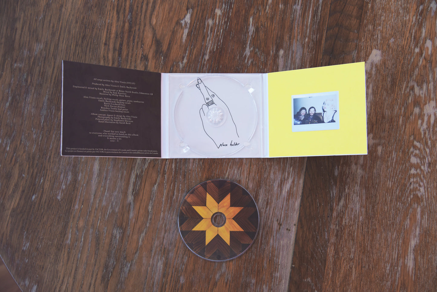Inside look at VISSIA Place Holder CD artwork; illustration of fingers crossed; polaroid photo of three friends sitting on a couch with glitter on their cheeks - the photo is against a bright yellow background